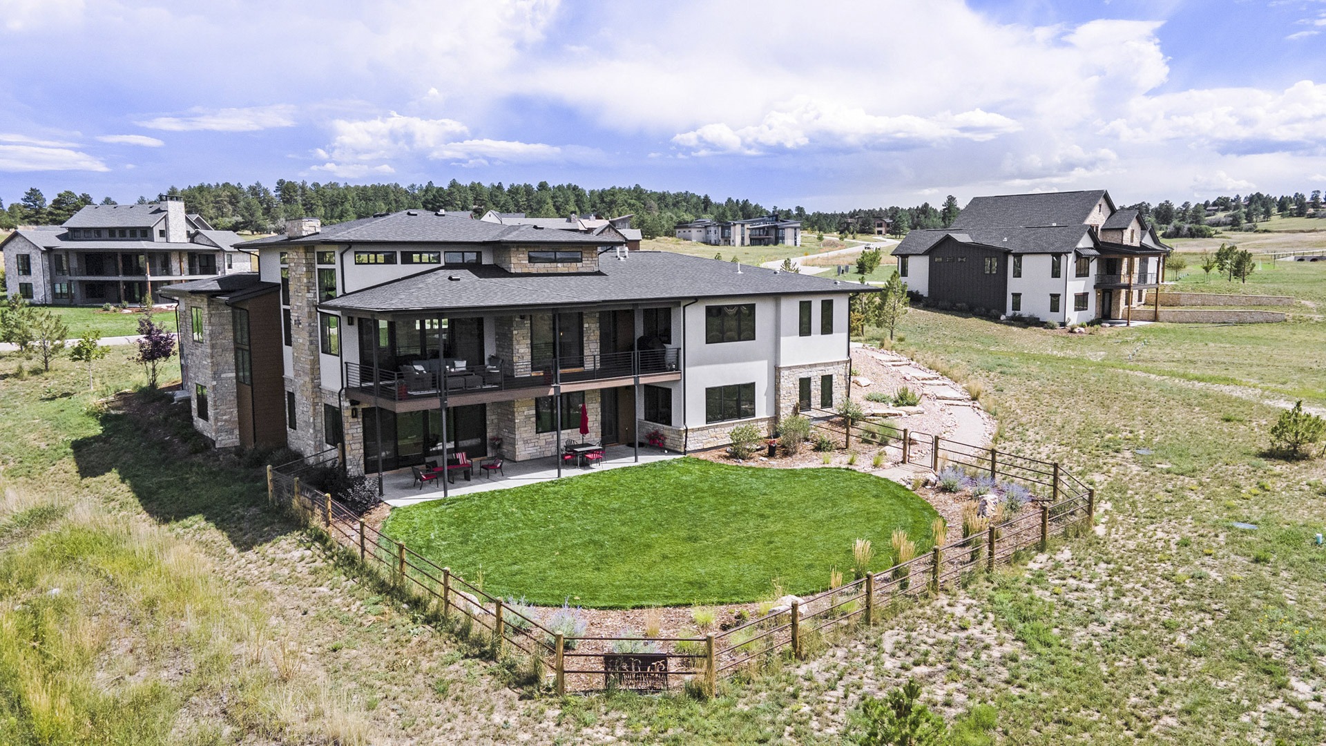 Modern luxury ranch home with a walkout basement, large deck, spacious patio, and a lush green lawn.