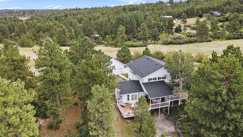 High-angle aerial drone image of the backyard of a luxury two-story home, showcasing a large deck and views of the area in front of the home.