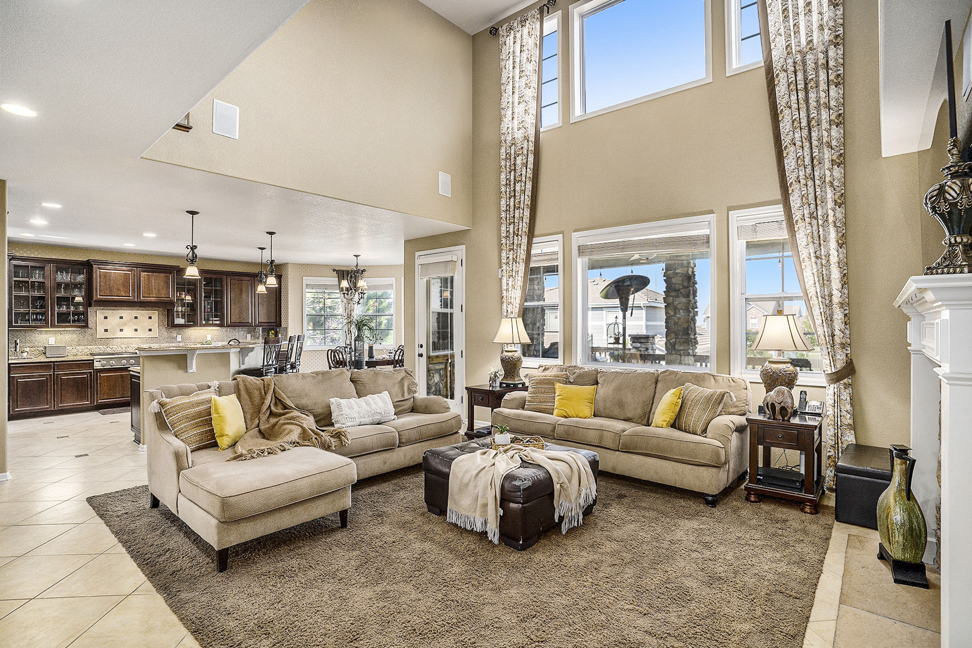 Open living room with tall ceilings, a fireplace, and views into the luxury kitchen.