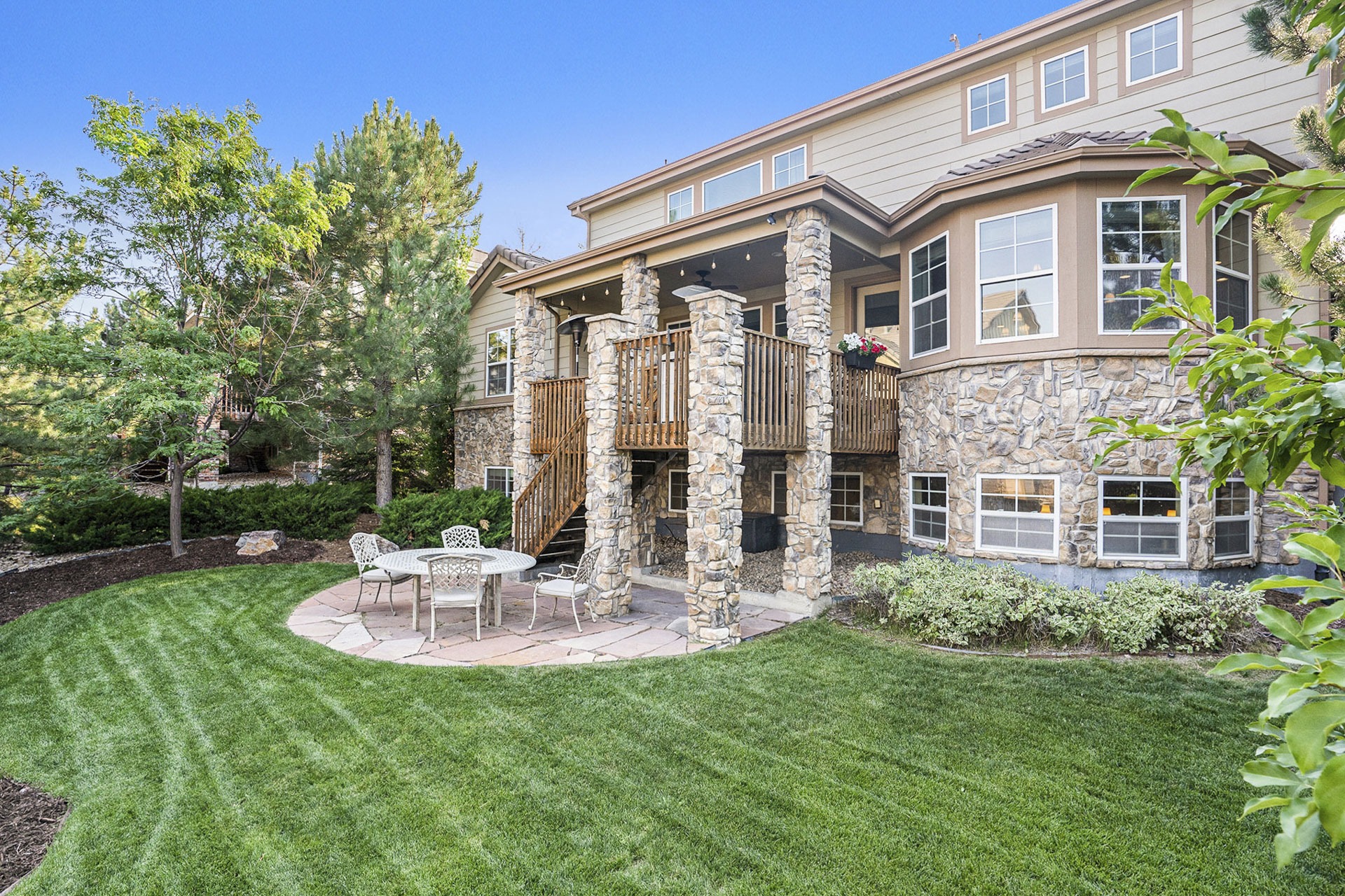 Backyard of a luxury two-story home with landscaping, a patio, and access to the main floor deck.