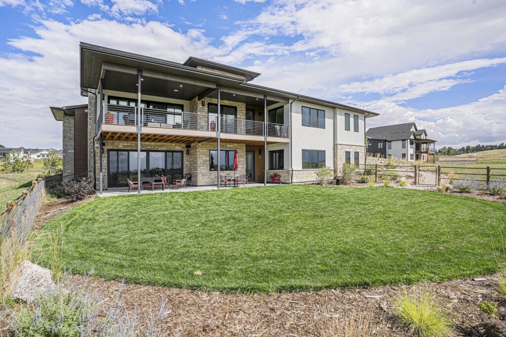 Modern luxury ranch home with a walkout basement, large deck, spacious patio, and lush green lawn.