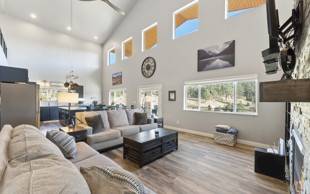 Living room of a newly built mountain home in Colorado with a fireplace, natural light, and an open kitchen in the background.
