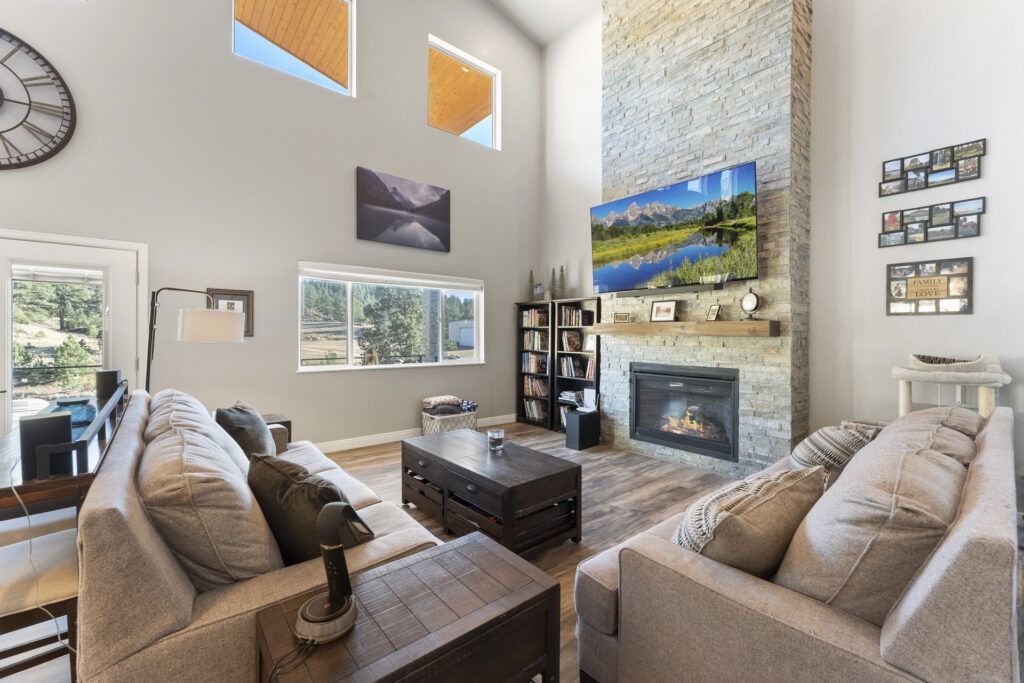 HDR image of the living room in a newly built Colorado mountain home with a fireplace, vaulted ceilings, and several windows.