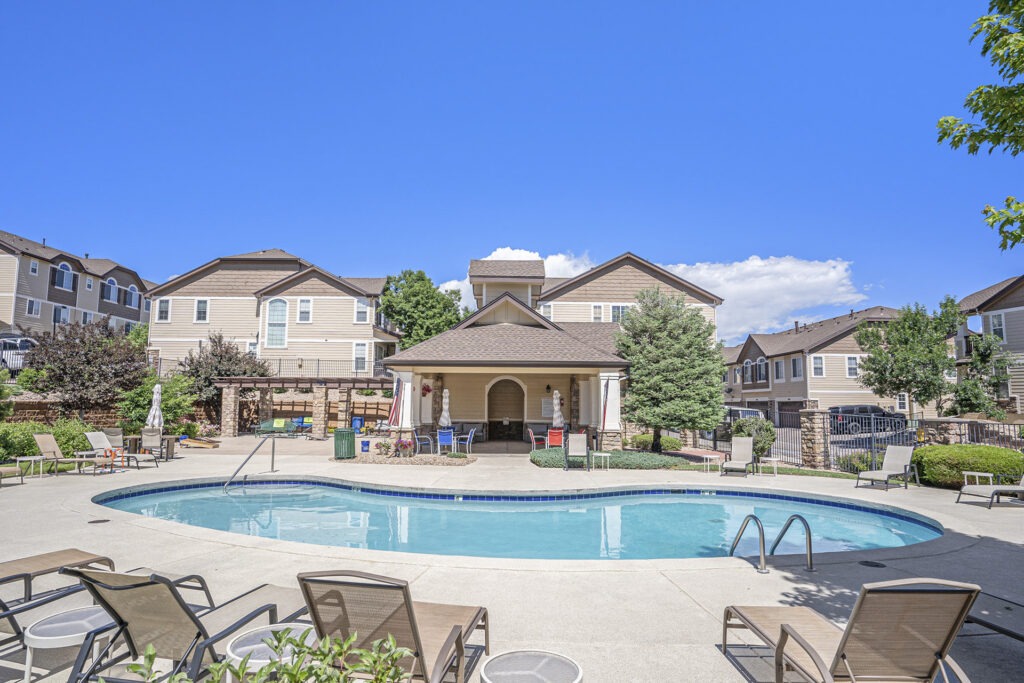 Community pool at a condo complex with a hot tub, lounge chairs, and condo buildings in the background.