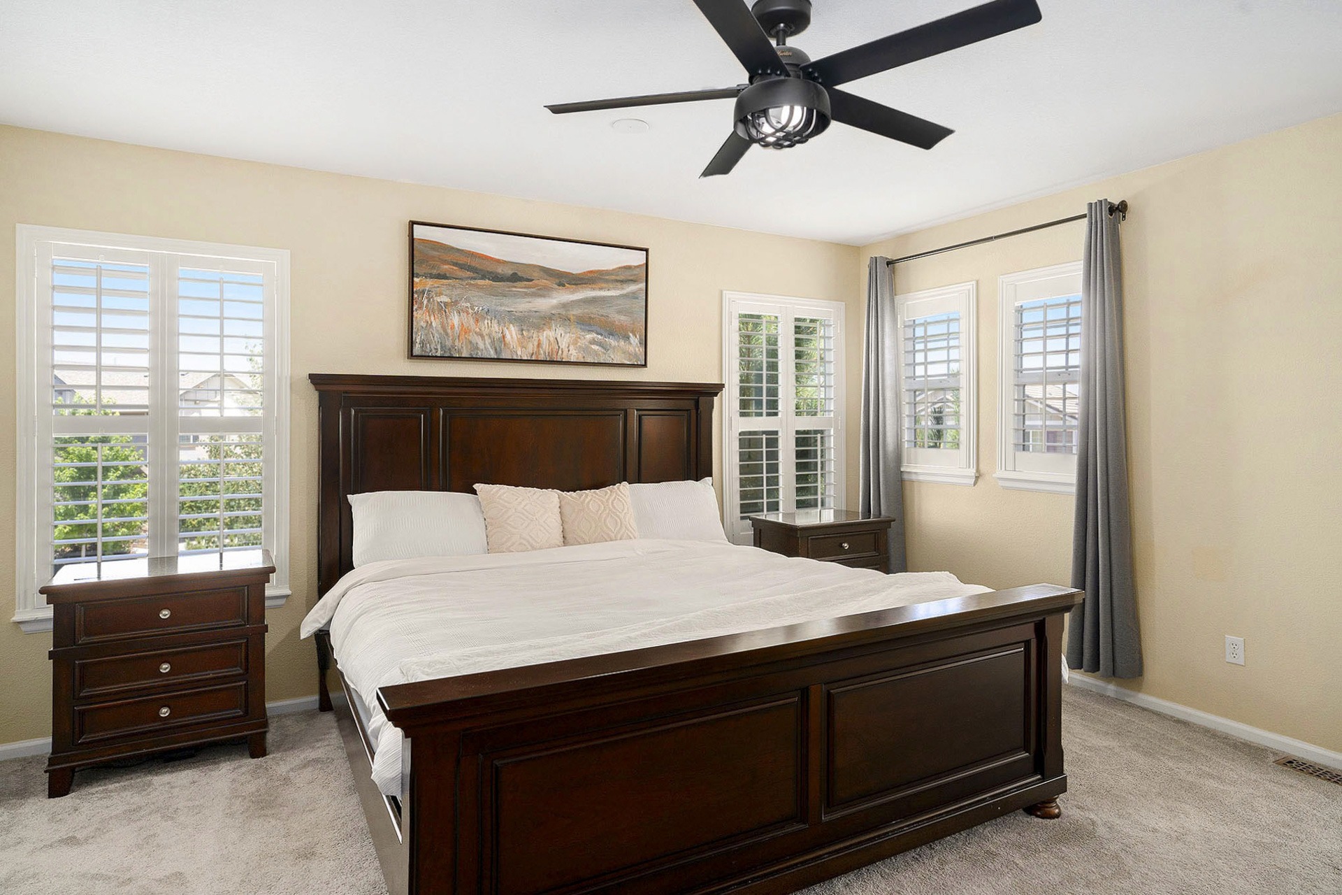Modern bedroom with abundant natural light, a sleek ceiling fan, and plantation shutters on the windows.