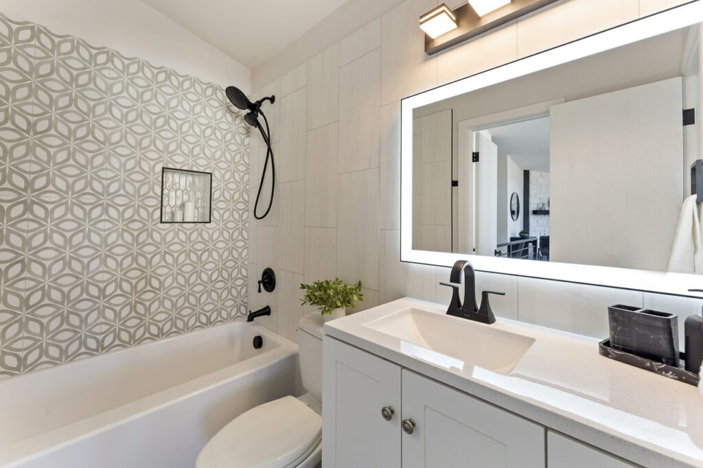 Updated full bathroom with a shower and tub combination, a lighted vanity mirror, and unique tile work in the shower area.