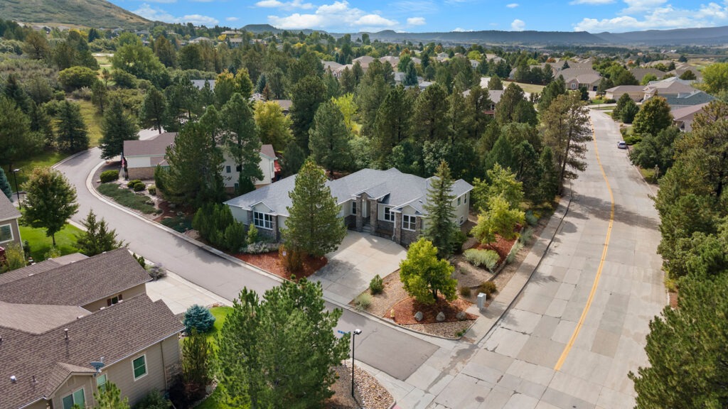 Aerial drone photo of a luxury Denver home on a corner lot surrounded by trees with mountain views in the background