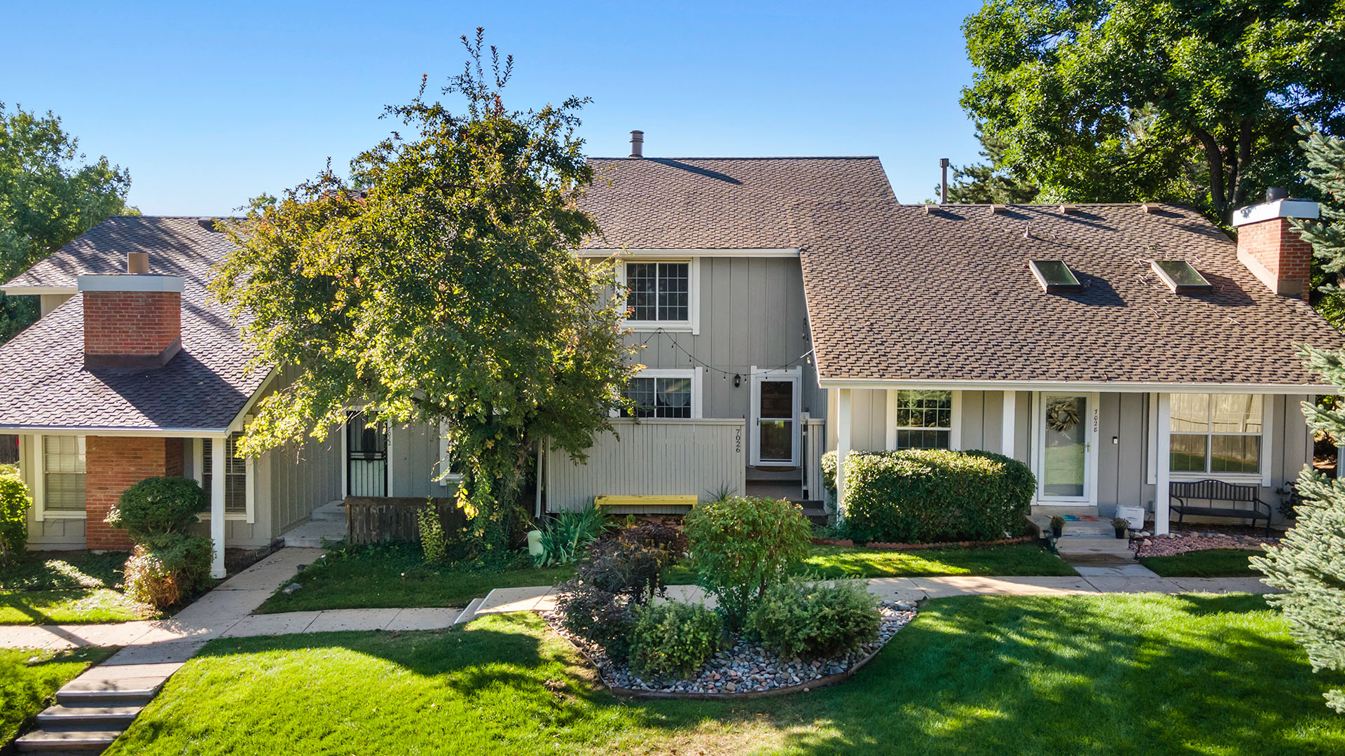 Aerial drone photo of a two-story Denver townhome with enclosed front porch overlooking green space and professional landscaping